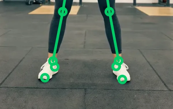 Close-up of a FormLens analysis replay filmed front-on: the green skeleton overlay marks the knee, ankle, heel and toe of each foot of a lifter standing on a gym floor.